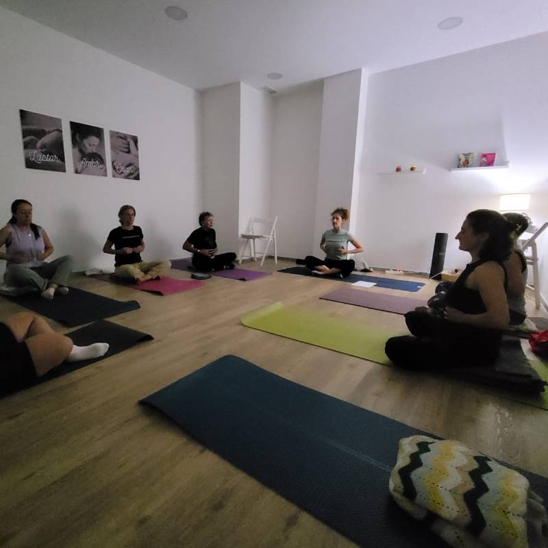 Grupo de mujeres en una clase presencial de yoga femenino, sentadas en meditación